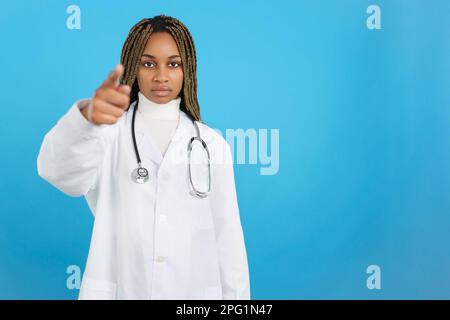 Ernsthafte afrikanische Ärztin mit Uniform, die nach vorne zeigt Stockfoto