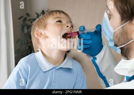 Der Junge bekommt Polio-Tropfen. Arztmachen zum Kind orale Schutzimpfung gegen Infektionen. Kleiner blonder Haarjunge im Krankenhaus. Kindergesundheitsfürsorge und Kinderkrankheiten Stockfoto