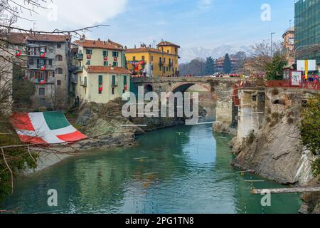 Ivrea, Italien - 19. Februar 2023: Blick auf die alte Brücke (Ponte Vecchio) mit Menschenmassen während des historischen Karnevals von Ivrea, Piemont, Norditalien Stockfoto