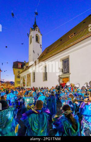 Luzern, Schweiz - 20. Februar 2023: Musiker in Kostümen und Menschenmassen, in der Nähe der St. Peter Chapel, bei Sonnenaufgang, Teil der Fasnacht Carniva Stockfoto