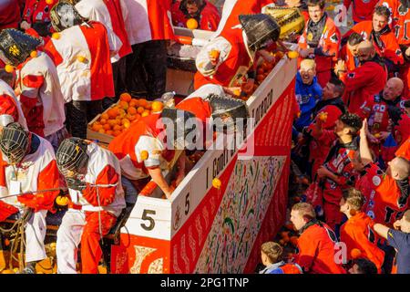 Ivrea, Italien - 19. Februar 2023: Gruppen in traditionellen Dressings und Menschenmenge mit roten Hüten nehmen an der Schlacht der Orangen Teil, Teil des Historors Stockfoto