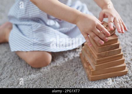 Outface Kind spielt eine hölzerne Pyramide, während es auf einem Teppich sitzt Stockfoto