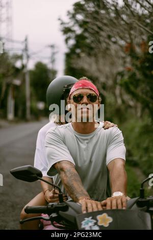 Ein Mann mit rotem Bandana fährt in Bali mit dem Fahrrad. Tropischer Lebensstil. Stockfoto