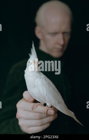 Ein Albino mit einem weißen Papagei auf dunklem Hintergrund Stockfoto