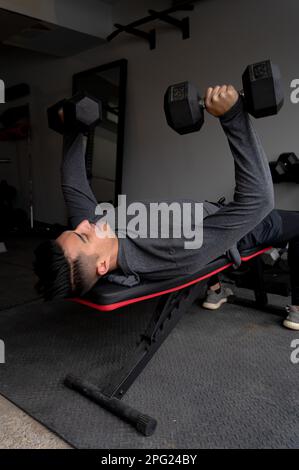 Young man Bench drückt Kurzhanteln im Fitnessstudio in der Hauswerkstatt Stockfoto