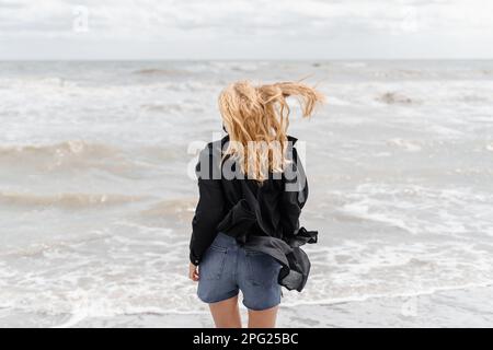 Traumhafte junge blonde Frau mit langen, welligen Haaren am Strand Stockfoto