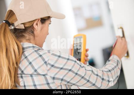 Frau, die einen Lichtschalter mit einem Multimeter testet Stockfoto