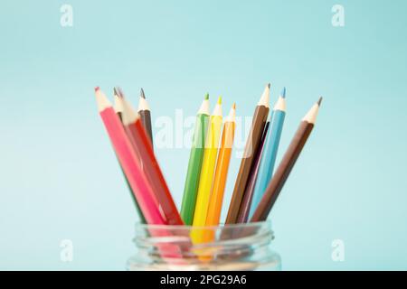 Mehrfarbige Bleistifte in einem Glasbehälter auf blauem Hintergrund. Stockfoto