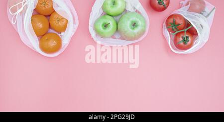 Apfel, Tangerinen und Tomaten in wiederverwendbaren Einkaufstaschen auf pinkfarbenem Hintergrund. Das Konzept der Abfallvermeidung und des umweltfreundlichen Lebensstils. Kein Plastik. Obere V-Achse Stockfoto