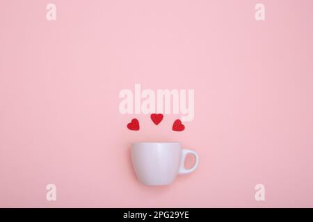 Kaffeetasse und rote Holzherzen auf rotem Hintergrund. Das Konzept von Valentinstag, Liebe, Verabredung und Hochzeit. Symbol für ein romantisches Geschenk oder eine Ehe Stockfoto