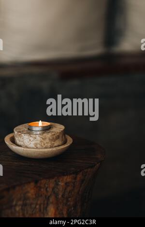 Eine brennende Kerze in einem Marmorstand auf einem Holztisch. Natürliche Details im Innenraum. Braunes Beige Stockfoto