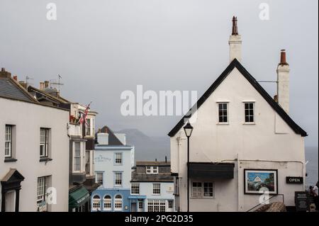 Die Gebäude am Fuße der Lyme Regis High Street wurden an einem nebligen Tag aufgenommen und blickten auf das Meer und die Hügel in der Ferne. Stockfoto