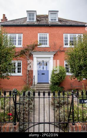 Ein typisches Dorset-Haus in England. Mit terrakottafarbenen Außenwänden, einer lilafarbenen Tür und einem formellen Garten und Vorderweg und Tor. Stockfoto