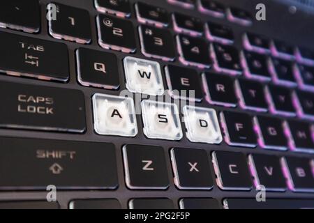 Spieletasten mit rosafarbenem violettem Farbverlauf und verschwommenem Hintergrund. Leistungsstarke Nahaufnahme der Notebook-Tastatur in dunkler Farbe. Technik, IT, E-Sport, Computerwissenschaft zurück Stockfoto