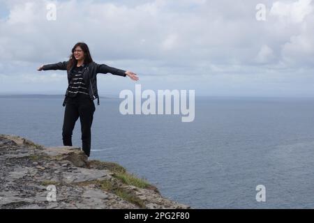 Junge Frau, die am Klippenrand in Cliffs of Moher, irland, posiert Stockfoto