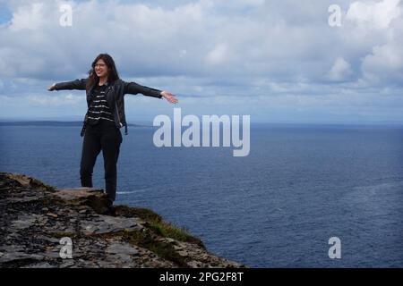 Junge Frau, die am Klippenrand in Cliffs of Moher, irland, posiert Stockfoto