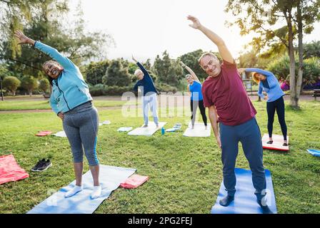 Multiethnische Senioren, die Stretching-Übungen im Freien mit Stadtpark im Hintergrund machen - gesunder Lebensstil und fröhlicher Lebensstil älterer Menschen con Stockfoto