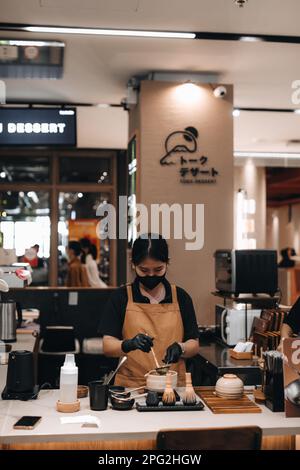 Junge Frau mit schwarzer Maske bereitet japanischen Matcha-Tee zu Stockfoto