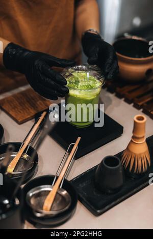 Zubereitung von japanischem grünem Tee von Matcha. Weibliche Hände, Plastikglas, traditionelle organische Utensilien. Stockfoto