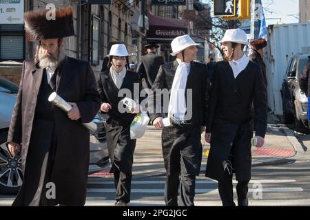 Eine Purim-Straßenszene in Brooklyn mit einem Mann in einem Shtreimal und Jungs in Kostümen. Stockfoto