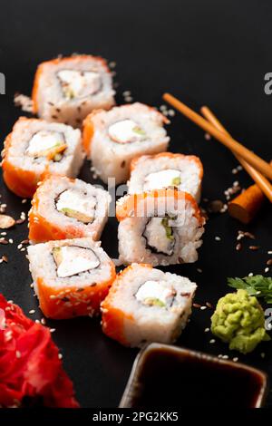 Die Auswahl verschiedener japanischer Sushi- und Brötchensorten. Auf dunklem rustikalem Hintergrund. Rollt auf dunklem Hintergrund. Meeresfrüchte mit Stäbchen. Stockfoto