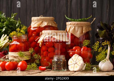 Tomatenkonserven in geschlossenen Gläsern mit Gewürzen auf Holzhintergrund. Tomaten für den Winter ernten. Tomaten aus der Dose mit Knoblauch, Pfeffer, Dill Stockfoto