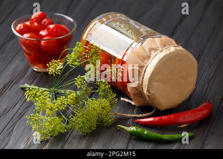 Tomaten in Dosen und Gurken in einem Glas. Marinierte Tomaten in einer Schüssel. Eingelegte Tomaten mit Chili, Dill und Knoblauch. Stockfoto