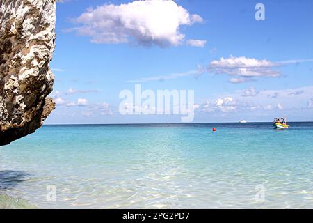 Eine ruhige Meereslandschaft mit einem kristallklaren blauen Ozean und einem kleinen Boot, das in Tulum, Mexiko, schwimmt Stockfoto