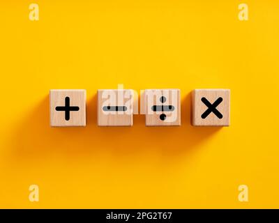 Symbole für grundlegende mathematische Operationen. Plus, Minus, Multiplikation und Teilung von Symbolen auf Holzwürfeln auf gelbem Hintergrund. Mathematik- oder Mathematikunterricht und Stockfoto