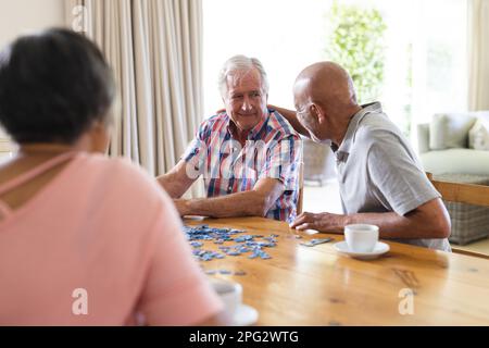 Eine glückliche Gruppe verschiedener Senior-Freunde, die am Tisch sitzen und Puzzle spielen Stockfoto