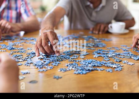 Hände von verschiedenen Senior-Freunden, die am Tisch sitzen und Puzzle-Puzzle spielen Stockfoto