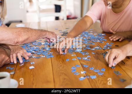 Hände von verschiedenen Senior-Freunden, die am Tisch sitzen und Puzzle-Puzzle spielen Stockfoto