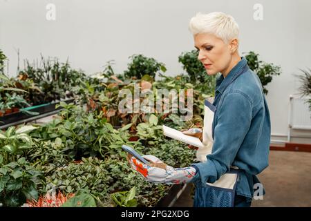 Heimpflanzenzucht, Gartenarbeit, Hausfrau, online arbeitender Social-Media-Influencer. Glückliche, wunderschöne Blumenbloggerin, die mit Plan fotografiert wurde Stockfoto