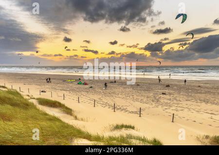 Kitesurfen bei Sonnenuntergang von den Dünen aus gesehen. Kite Surfen Leute Aktivität am Strand unter Setting Su in Wijk aan Zee, Niederlande. Stockfoto