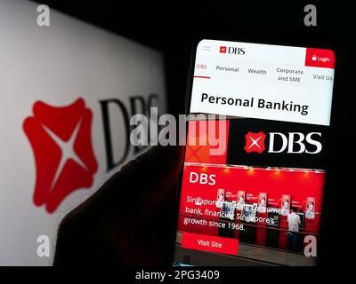 Person, die ein Smartphone mit einer Website des Finanzunternehmens DBS Bank Limited in Singapur auf dem Bildschirm mit Logo hält. Konzentrieren Sie sich auf die Mitte des Telefondisplays. Stockfoto