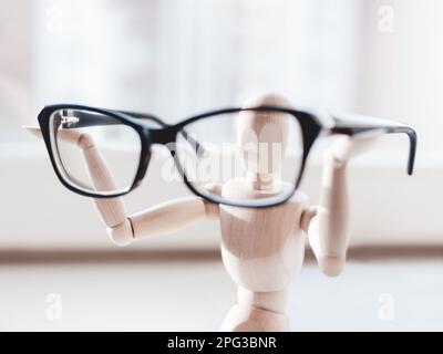 Holzpuppe mit Brille in den Händen. Die Schaufensterpuppe zeigt eine Brille, um das Leben bei schlechter Sicht zu trösten. Miniaturmodell des Menschen Stockfoto