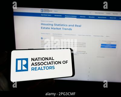 Person, die ein Mobiltelefon mit dem Logo der US National Association of Realtors (NAR) auf dem Bildschirm vor der Webseite hält. Konzentrieren Sie sich auf das Display des Telefons. Stockfoto