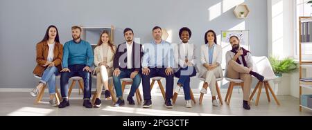 Porträt einer Gruppe von Personen, die auf Stühlen in Reihe sitzen und Zuhörer oder Kandidaten sind. Stockfoto