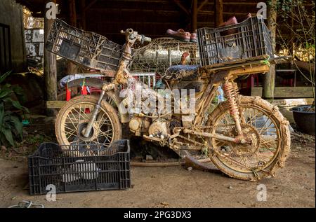 Ein verprügelter, verwüsteter und sehr schlammiger alter Motorradroller, der in einem Café in Dam Rong, Provinz Lam Dong, Vietnam, geparkt hat. Stockfoto