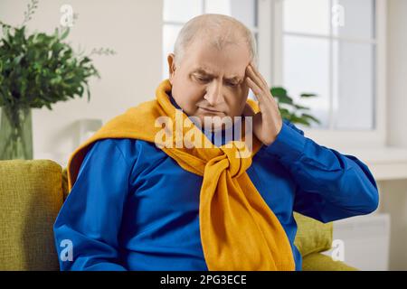 Porträt eines grauhaarigen älteren Mannes mit Kopfschmerzkrankheit, der zu Hause auf dem Sofa sitzt. Stockfoto
