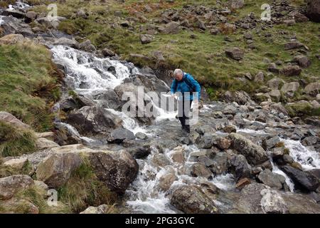 Man (Hiker) geht auf dem Gatherstone Beck Wasserfall am Gatherstone Head auf dem Black Sail Pass Path im Mosedale Valley, Lake District National Park. Stockfoto