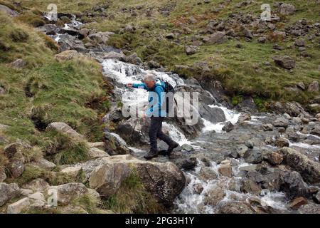 Man (Hiker) geht auf dem Gatherstone Beck Wasserfall am Gatherstone Head auf dem Black Sail Pass Path im Mosedale Valley, Lake District National Park. Stockfoto