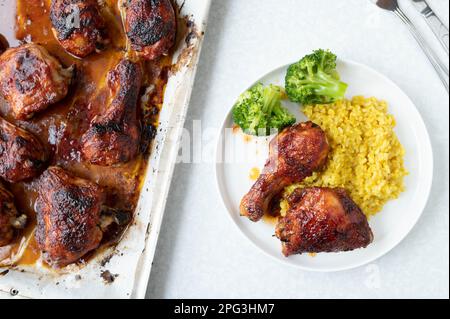 Gebackenes und glasiertes Barbecue-Hähnchen mit Pilau-Reis und Brokkoli auf weißem Hintergrund von oben Stockfoto