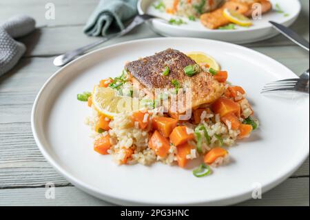 Gebratener Lachs mit Haut serviert mit braunem Reis und Gemüse auf einem Teller Stockfoto