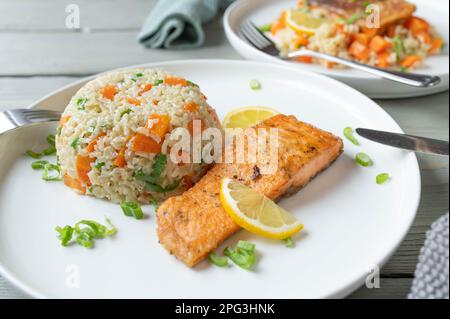 Gebratener Lachs mit braunem Reis, Erbsen, Karotten und Lauch auf einem Teller Stockfoto