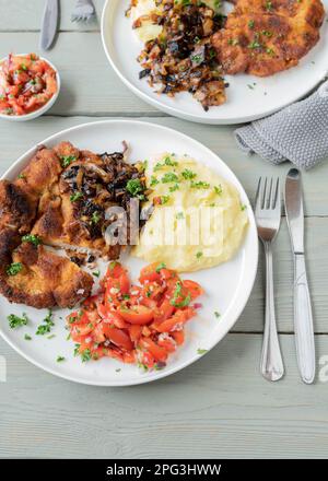 Schweineschnitzel mit gerösteten Zwiebeln, Kartoffelpüree und Tomatensalat auf einem Teller Stockfoto