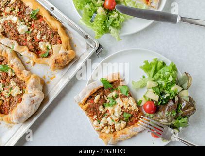 Türkische Pide oder Fladenbrot mit Hackfleisch, Fetakäse auf weißem Küchentisch mit Teller und Leinenpfanne Stockfoto