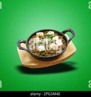 Schwimmender Palak-Paneer in einer kleinen Pfanne auf grünem verlaufendem Hintergrund gebacken Stockfoto