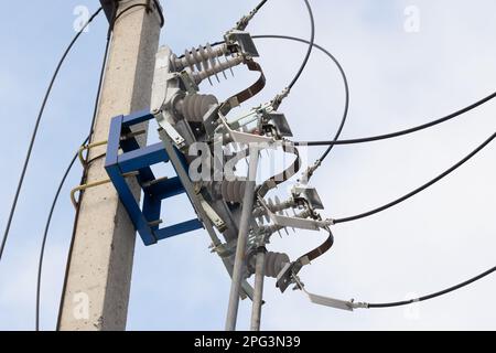 Der Trennschalter für Hochspannungsleitungen, der an einem Betonmast montiert ist, befindet sich unter blauem Himmel Stockfoto