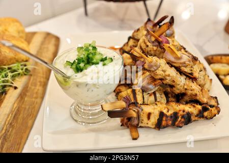Souvlaki-Spieße oder Kebabs von griechischem Huhn, die sich hoch auf einem weißen Teller mit einer Schüssel Tzatziki-Sauce stapeln Stockfoto